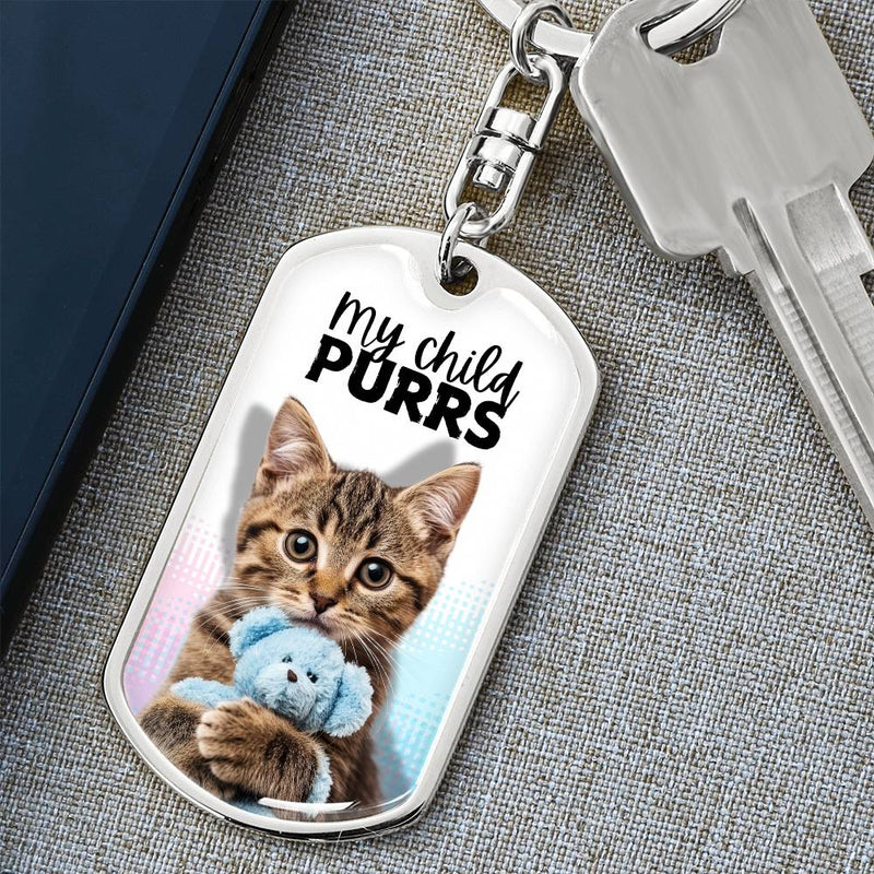 White and silver dog tag shaped keychain with a kitten holding a blue blanket.