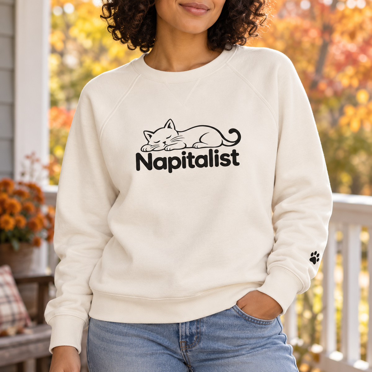Woman wearing a cream Napitalist sweatshirt with a black sleeping cat design and left-sleeve paw print.