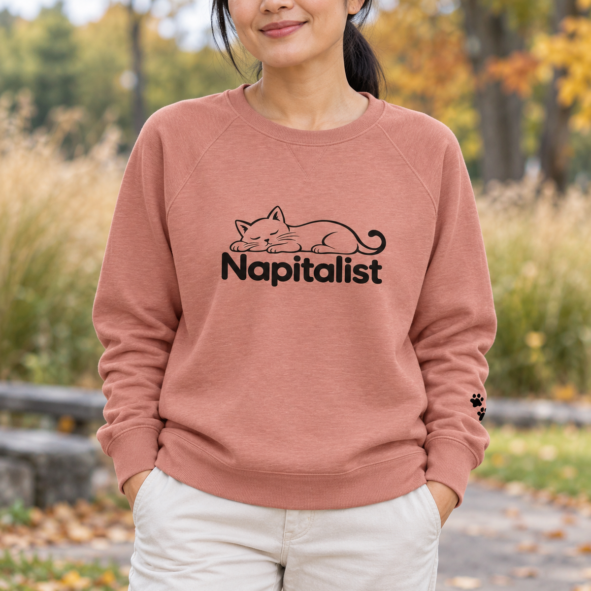 Woman wearing a dusty peach Napitalist sweatshirt with a sleeping cat graphic.
